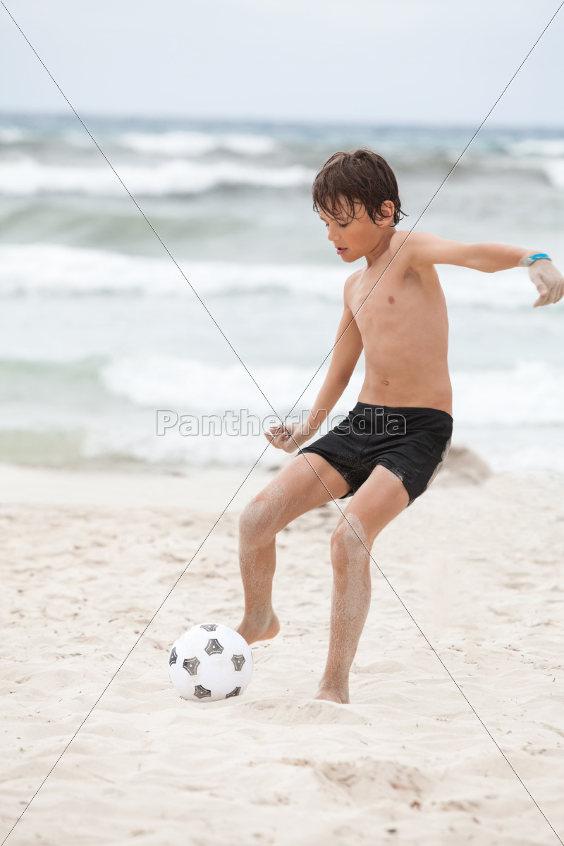 Imagem de crianças jogando bola na beira da praia.